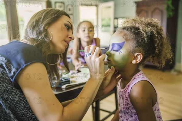 Mother painting face of daughter in living room