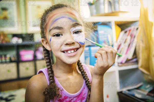 Mixed race girl painting her face in bedroom