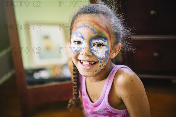 Mixed race girl painting her face in bedroom