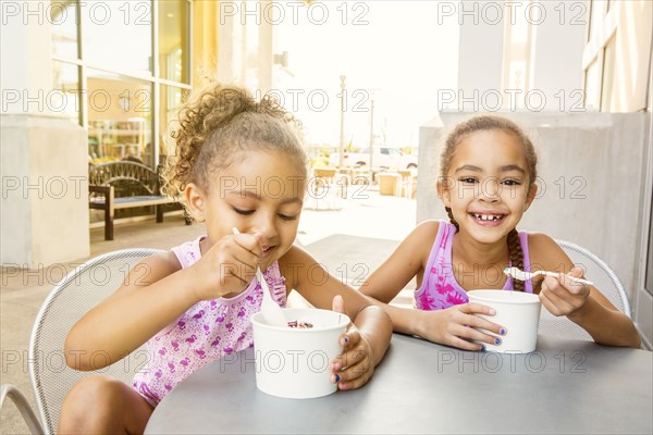 Mixed race sisters eating ice cream at outdoor cafe