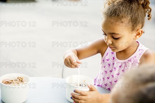 Mixed race girl eating ice cream at outdoor cafe