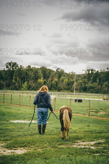 Caucasian woman walking miniature horse on ranch