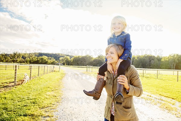 Caucasian mother carrying daughter on shoulders on rural road