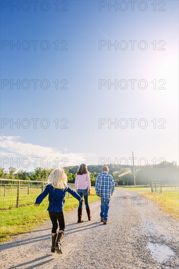 Caucasian children walking on dirt road on ranch