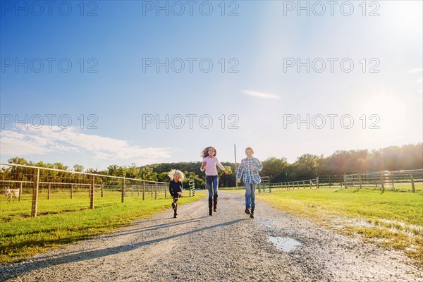 Caucasian children walking on dirt road on ranch