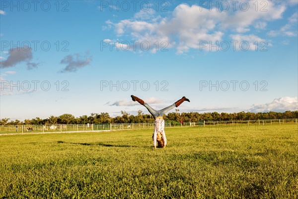 Caucasian girl doing headstand in field on ranch