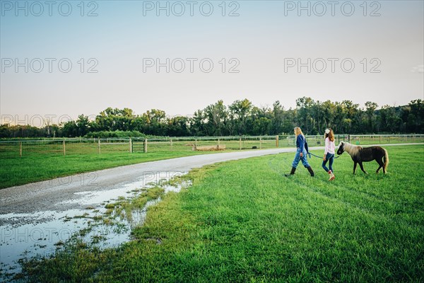 Caucasian mother and daughter walking miniature horse on farm