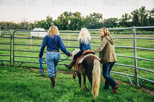 Three generations of Caucasian women walking miniature horse on farm