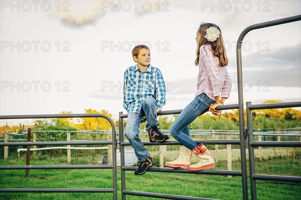 Caucasian children sitting on fence on farm