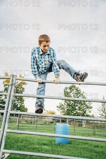 Caucasian boy climbing fence on farm