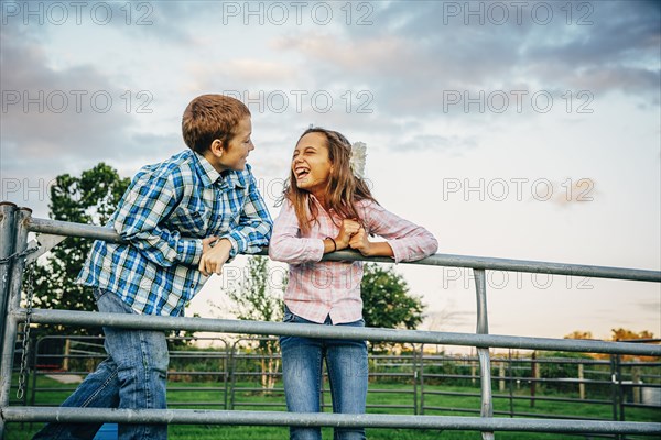 Caucasian children standing on fence on farm