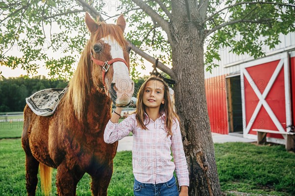 Caucasian girl walking horse outside barn on farm