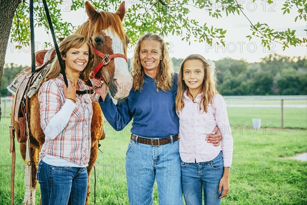 Three generations of Caucasian women standing near horse on farm