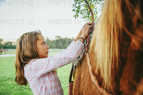 Caucasian girl fastening saddle on horse