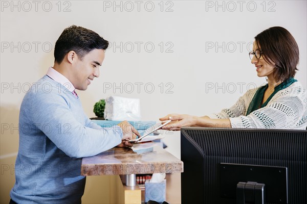 Secretary offering tablet to businessman in office lobby