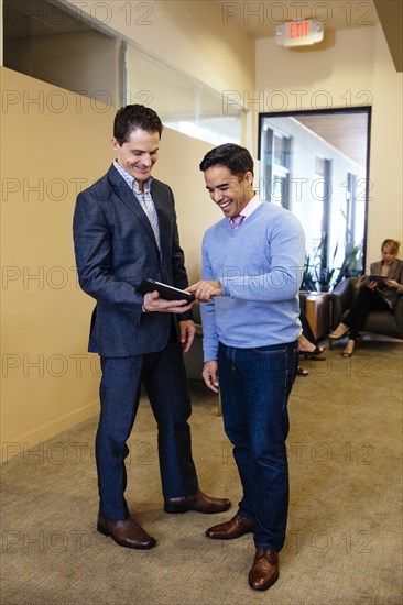 Businessmen using digital tablet in office hallway