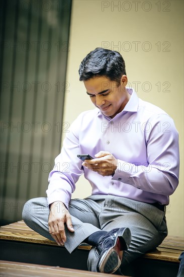 Mixed race businessman using cell phone in office courtyard