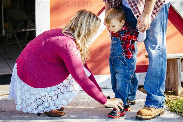 Caucasian mother tying shoes of son outside barn