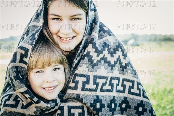 Caucasian sisters wrapped in blanket on farm