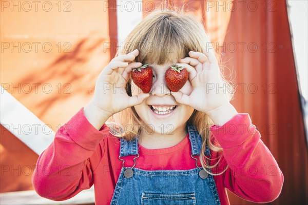 Caucasian girl holding strawberries over eyes