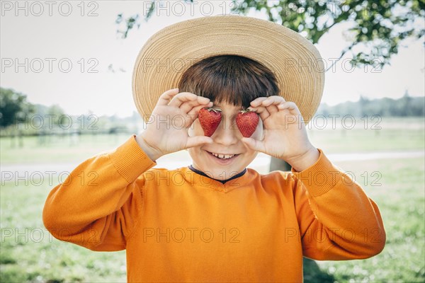 Caucasian boy holding strawberries over eyes on farm