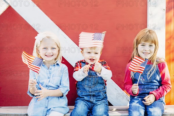 Caucasian children waving American flags outside barn