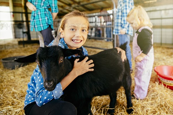 Caucasian girl petting goat in barn