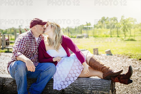 Caucasian couple kissing on wooden log in park
