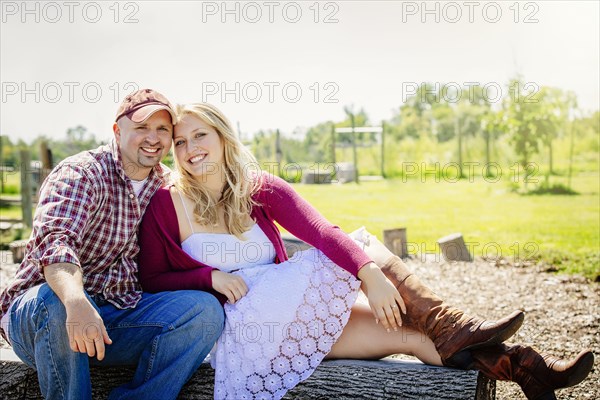 Caucasian couple kissing on log in park