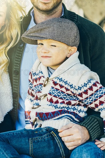 Caucasian boy winking on lap of father