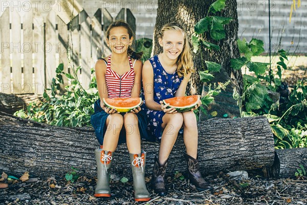 Caucasian girls eating watermelon under tree