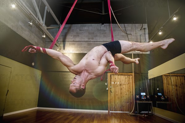 Caucasian acrobat hanging from ropes in studio