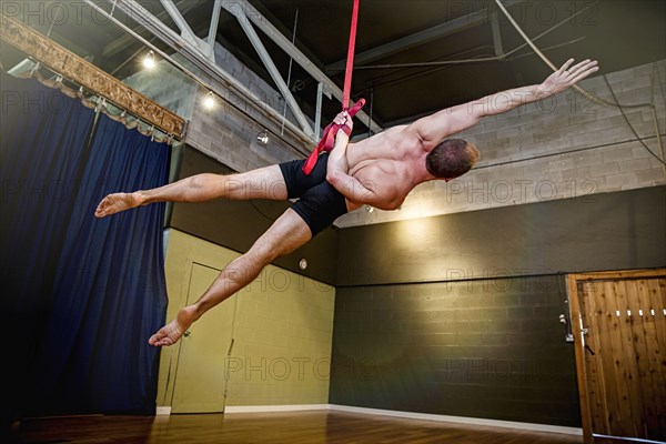 Caucasian acrobat hanging from ropes in studio