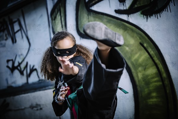 Mixed race girl kicking in martial arts uniform and mask