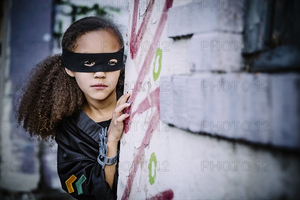 Mixed race girl in mask peeking around corner