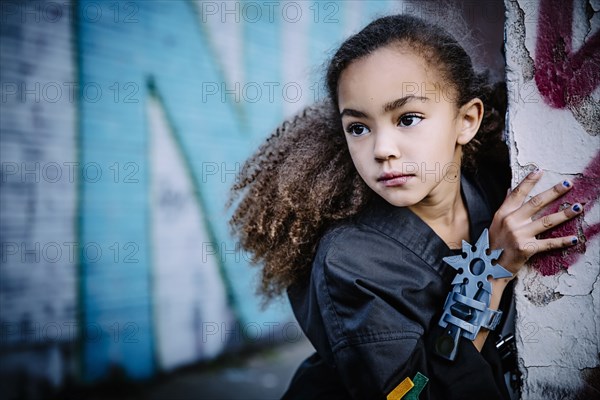 Mixed race girl in martial arts uniform with throwing star peeking around corner