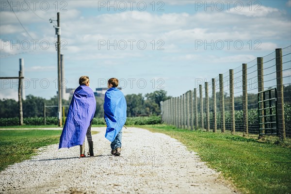 Caucasian children wearing capes on dirt road