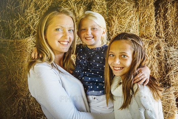 Caucasian mother and daughters smiling near haystacks