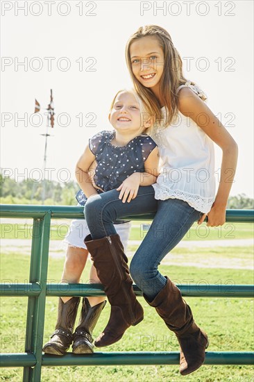 Caucasian sisters smiling on gates near farm field