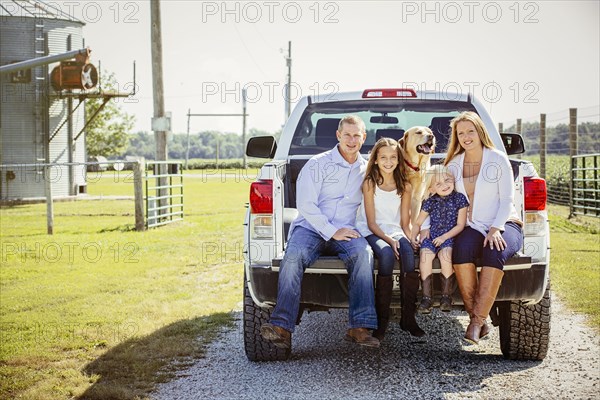 Caucasian family and dog sitting in truck bed on farm