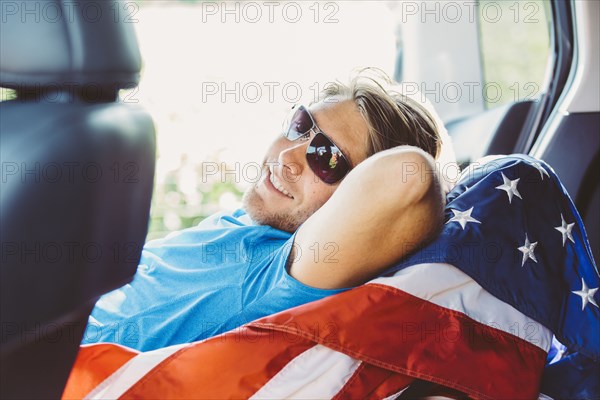 Caucasian man laying on American flag in car