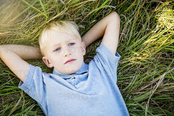 Serious Caucasian boy laying in tall grass