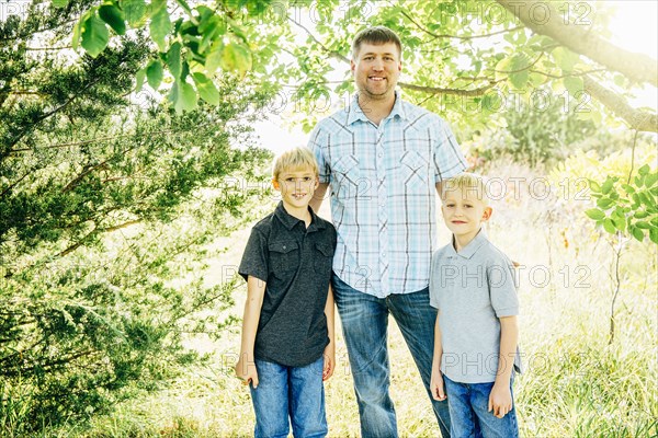 Caucasian father and sons smiling under trees