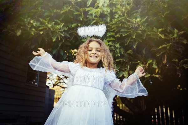 Mixed race girl wearing angel costume in backyard