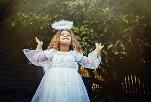 Mixed race girl wearing angel costume in backyard