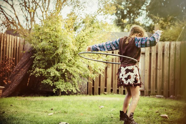 Mixed race girl in cowboy costume spinning plastic hoop in backyard