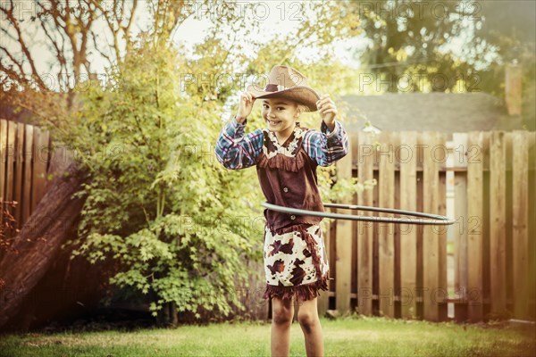 Mixed race girl in cowboy costume spinning plastic hoop in backyard
