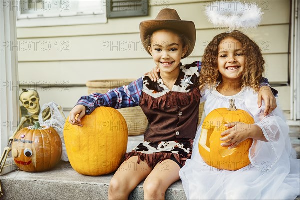 Sisters wearing Halloween costumes with jack-o-lanterns on porch