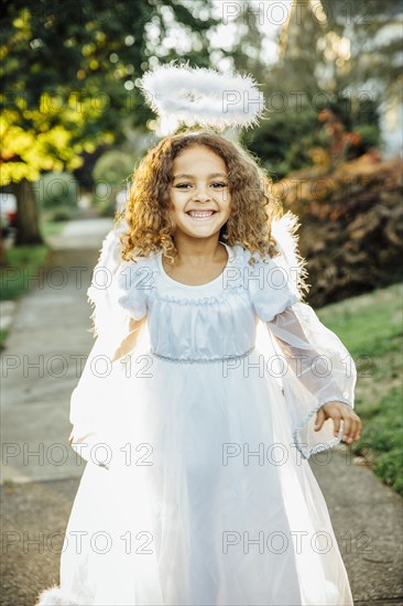 Mixed race girl wearing angel costume on sidewalk