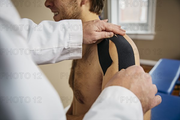 Caucasian doctor applying tape to shoulder of patient